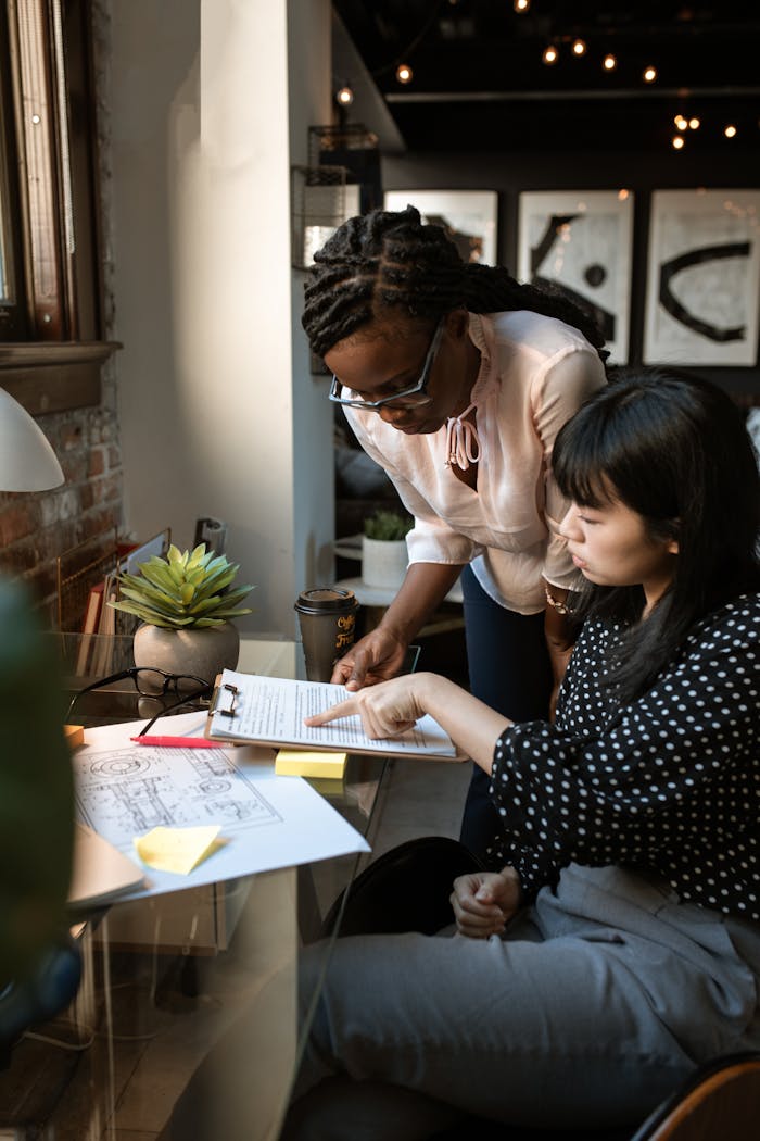 Two women working together at a desk, reviewing documents in a modern office environment.